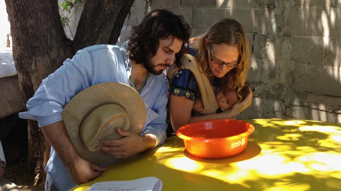 An image of a man and woman (holding a child) looking into a bowl of water An image of a man and woman (holding a child) looking into a bowl of water