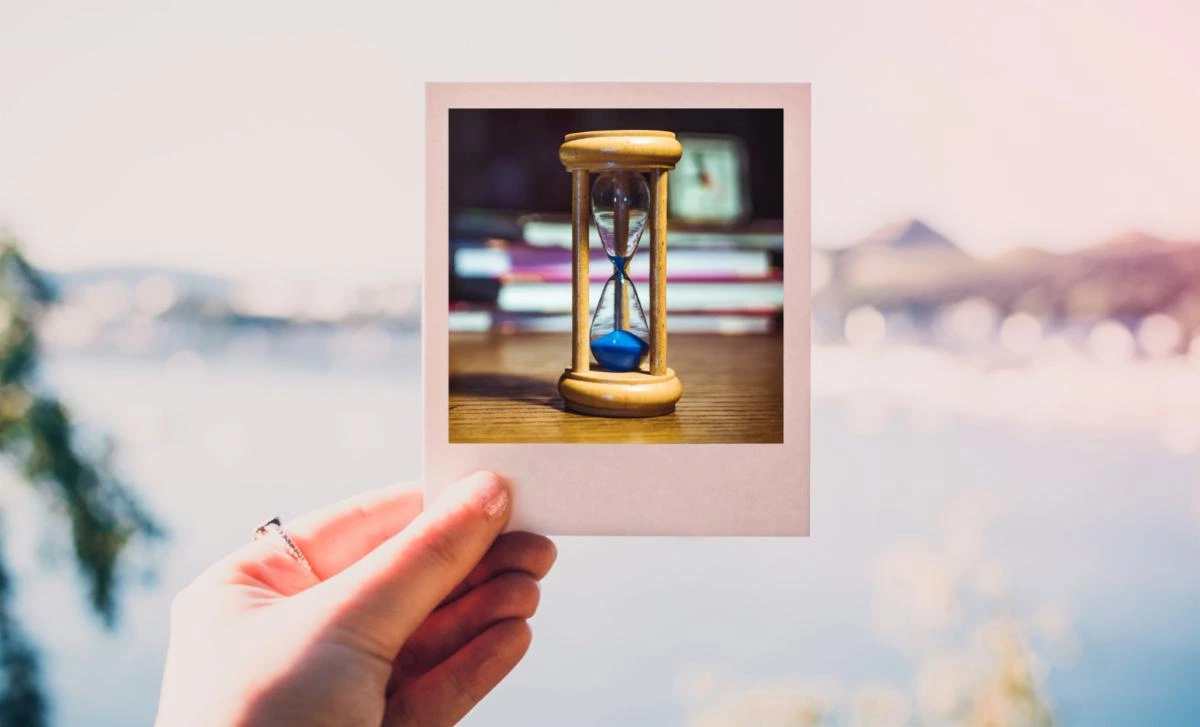 a hand holding a Polaroid image of an hourglass a hand holding a Polaroid image of an hourglass